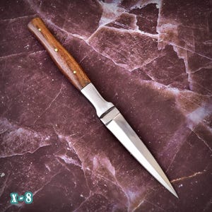May include: A handcrafted dagger with a polished steel blade and a wooden handle. The handle is a rich brown color, accented with small brass rivets. The blade is sharp and pointed, and the dagger has a silver metal bolster. The text "X-8" is in the bottom left corner.