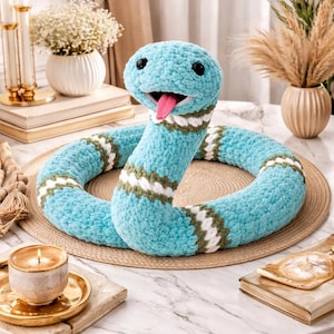 Könnte beinhalten: Ein kuscheliges, türkisfarbenes Schlangenspielzeug mit einem lächelnden Gesicht und einer rosa Zunge. Der Körper der Schlange ist mit weißen und olivgrünen Streifen versehen. Das Spielzeug besteht aus weichem, strukturiertem Material.