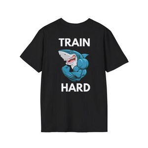 May include: Black t-shirt with a cartoon shark flexing its biceps. The shark is blue and white with a red mouth. The text "TRAIN HARD" is above and below the shark in white block letters.