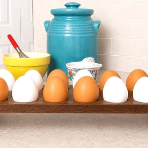 May include: A rectangular dark brown wooden egg holder with circular cutouts, containing a mix of twelve brown and white chicken eggs. The holder features arched side panels with circular openings for handles, providing a stable base.