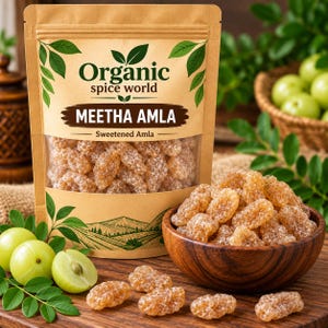 Könnte beinhalten: Ein beigefarbener Standbeutel mit der Aufschrift Organic Spice World Meetha Amla Sweetened Amla, der getrocknete, kandierte Fruchtstücke enthält. Eine Holzschale mit denselben süßen Amla-Früchten steht neben frischen Amla-Früchten und Blättern.
