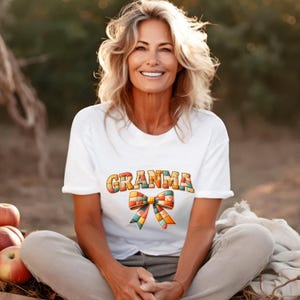 May include: White t-shirt with the word "Granma" in colorful, block letters and a matching bow graphic. The shirt is made of a soft material and is perfect for everyday wear.