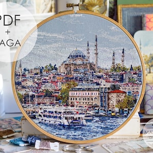May include: A circular wooden embroidery hoop containing a cross-stitch pattern of the Istanbul skyline, featuring the Suleymaniye Mosque, city buildings, and a boat on the water. The text PDF + SAGA is visible in the upper left corner of the image.