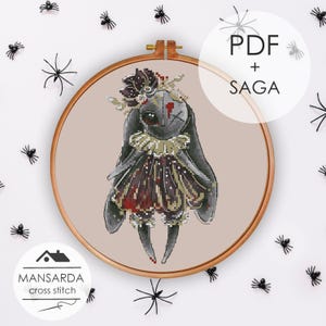 May include: A cross stitch pattern in a wooden hoop featuring a dark grey rabbit doll with long ears, a ruffled collar, and a red and black dress. The doll has one eye and a stitched cross over the other. Text reads PDF + SAGA and MANSARDA cross stitch.