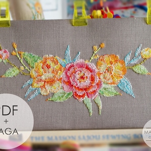 Peut inclure: Un motif de point de croix sur tissu gris représentant une fleur rose centrale entourée de deux fleurs orange, de feuilles vertes et de petits bourgeons jaunes. Un cercle blanc affiche le texte PDF + SAGA et le logo MANSARDA cross stitch.