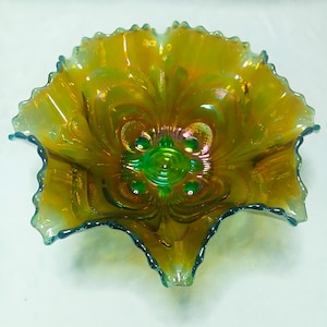 May include: A round glass bowl featuring an iridescent marigold finish with a vibrant green center. The bowl has a ruffled, scalloped edge and a molded pattern of raised circular dots and curved lines radiating from the base to the rim.