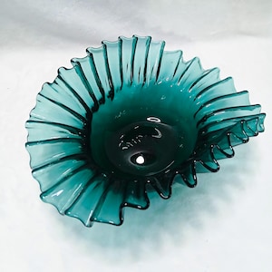 Può includere: Una ciotola in vetro traslucido color verde acqua con un bordo ampio, arricciato e pieghettato che si allarga verso l'esterno. La ciotola presenta una base circolare liscia e profonda che si trasforma in una serie di pieghe verticali.