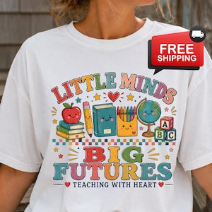 Peut inclure: Un t-shirt blanc avec un motif color&eacute; portant le texte LITTLE MINDS BIG FUTURES TEACHING WITH HEART. Le design comprend une pomme rouge, un crayon, un livre bleu, une bo&icirc;te de crayons, un globe et des cubes alphabet, tous avec des visages souriants.
