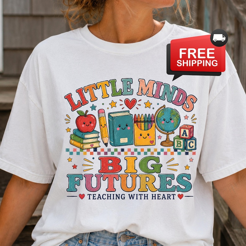 Peut inclure: Un t-shirt blanc avec un motif color&eacute; portant le texte LITTLE MINDS BIG FUTURES TEACHING WITH HEART. Le design comprend une pomme rouge, un crayon, un livre bleu, une bo&icirc;te de crayons, un globe et des cubes alphabet, tous avec des visages souriants.