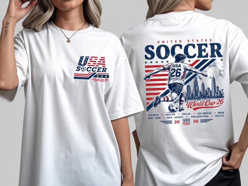May include: A white t-shirt featuring a small USA Soccer World Cup 26 logo on the front left chest. The back displays a large graphic of a soccer player, a city skyline, the text United States Soccer World Cup 26, and a list of host cities.