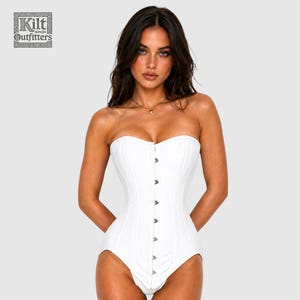 Op de afbeelding: Een wit strapless korset met een verticale rij zilverkleurige metalen sluitingen aan de voorzijde. Het kledingstuk heeft een gestructureerd, nauwsluitend ontwerp met zichtbare verticale naden. Het Kilt Outfitters logo staat linksboven.