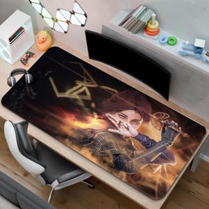 Peut inclure: Tapis de souris rectangulaire avec une illustration numérique d'une femme tenant une épée sur un fond enflammé. Le design utilise des nuances de marron, d'orange et de noir, avec des détails sur la tenue. Le tapis est posé sur un bureau en bois.