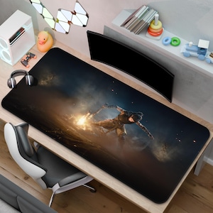 Könnte beinhalten: Ein großes, rechteckiges, schwarzes Gaming-Mauspad mit einem Krieger, der ein leuchtendes Schwert schwingt. Das Pad hat eine detaillierte Illustration mit einem dunklen, rauchigen Hintergrund. Das Pad liegt auf einem Holztisch.