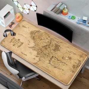 May include: A rectangular desk mat featuring a detailed, vintage-style map of Middle-earth printed in shades of tan and brown. The map includes intricate topographical illustrations, a compass rose, and text labels such as Middle-earth and Sundering Seas.