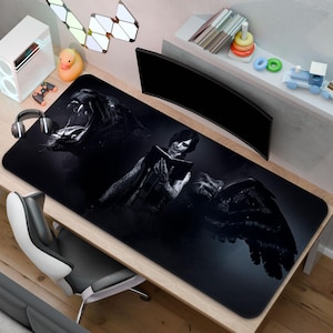 May include: Black and white desk mat with a detailed illustration of a roaring lion, a person reading a book, and a raven's wing. The rectangular mat is designed for gaming, enhancing the user's experience.