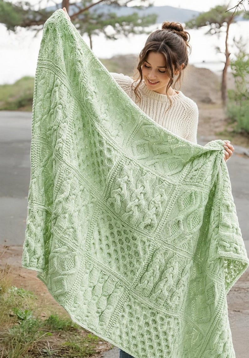 May include: A light green knitted blanket featuring a variety of textured patterns including cable stitches and honeycomb designs. The blanket is constructed from multiple square panels joined together in a grid, showcasing intricate yarn work.