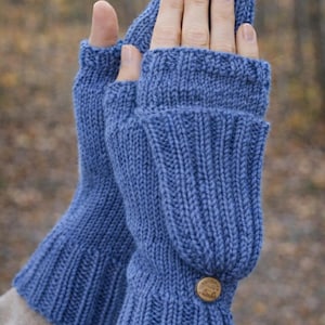 Könnte beinhalten: Ein Paar blaue Strick-Fäustlinge. Die Fäustlinge haben ein geripptes Bündchen und einen Knopfverschluss. Der obere Teil des Fäustlings kann zurückgeklappt werden, um die Finger freizulegen. Der Hintergrund ist unscharf.