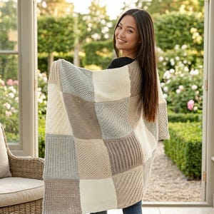May include: A rectangular knit blanket featuring a patchwork design of alternating squares in cream, light gray, and soft beige. The blanket displays a variety of textured stitch patterns, including ribbed, garter, and seed stitch, arranged in a grid.