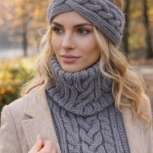 Pode incluir: Um conjunto de faixa de cabelo e gola cinza em malha de cabo. A faixa de cabelo apresenta um design trançado, e a gola tem um padrão de malha de cabo correspondente. O conjunto é feito de um material macio e quente, perfeito para o clima frio.