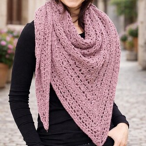 May include: A dusty rose-colored, crocheted shawl with a triangular shape. The shawl features an open, lacy design and is draped around the neck and shoulders. The garment is made of a soft, textured yarn, perfect for cool weather.