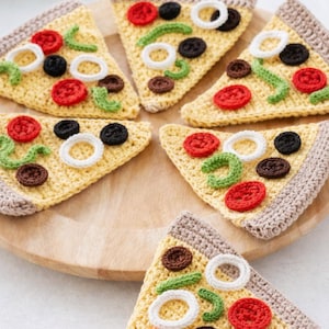 Puede incluir: Un conjunto de posavasos de ganchillo con forma de porción de pizza. Cada porción presenta una "corteza" amarilla con bordes marrones, y está cubierta con rodajas de tomate rojo, aceitunas negras, aros de cebolla blancos y pimientos verdes. Los posavasos están colocados en una bandeja de madera.