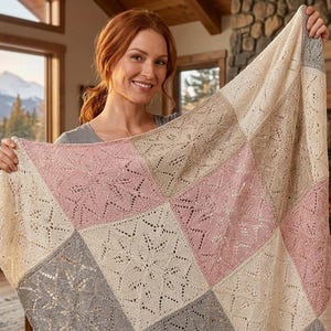 May include: A square-patterned knit blanket featuring alternating blocks of cream, soft pink, and light gray yarn. Each block displays a delicate, intricate lace-like star or floral motif created through openwork knitting techniques.