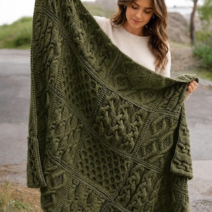 May include: An olive green knit blanket featuring a complex arrangement of raised cable stitch patterns and textured honeycomb panels. The rectangular textile displays a repeating grid of vertical and horizontal knit designs in a deep earthy tone.