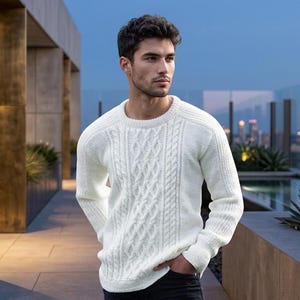 May include: A white long-sleeved jumper featuring a prominent vertical cable knit pattern on the front, a classic crew neckline, and ribbed cuffs. The garment is constructed with a textured knit design and is worn over dark-coloured trousers.