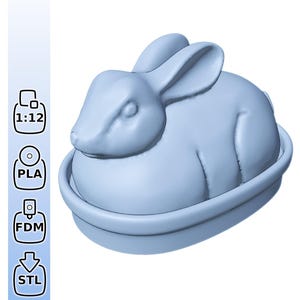 Könnte beinhalten: Eine hellblaue, 3D-gedruckte Hasenfigur, die in einer kreisförmigen Basis ruht. Der Hase hat detaillierte Merkmale, darunter lange Ohren und einen abgerundeten Körper. Das Bild enthält auch Symbole für 3D-Druckverfahren und einen Maßstab von 1:12.
