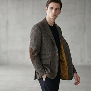 May include: A brown tweed blazer with brown suede elbow patches. The blazer has two front pockets and a gold-colored lining. The person is wearing a black shirt and navy blue pants.