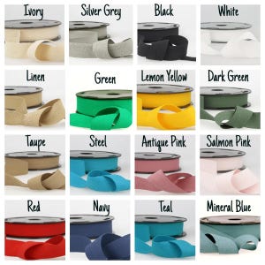 May include: A selection of ribbon spools in a range of colours: ivory, silver grey, black, white, linen, green, lemon yellow, dark green, taupe, steel, antique pink, salmon pink, red, navy, teal, and mineral blue. Each spool is labelled with its colour name.