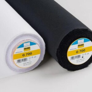 May include: Two rolls of fabric, one white and one black, are side by side. Each roll has a yellow and blue label with the text "G 700". The fabric is tightly rolled, showing the texture of the material.