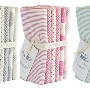 Peut inclure: Plusieurs paquets de tissu aux motifs et couleurs variés, dont des rayures, des pois et des étoiles. Chaque paquet est noué avec un ruban et une étiquette « Classic Basics ». Les couleurs de tissu incluent le gris, le rose et le turquoise.
