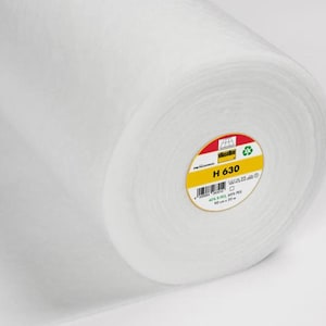 Może przedstawiać: Prezentowany jest zwój białej tkaniny, prawdopodobnie flizeliny lub waty. Rolka jest ciasno zwinięta, ukazując warstwy materiału. Widoczna jest żółto-czerwona etykieta z napisem "H 630".