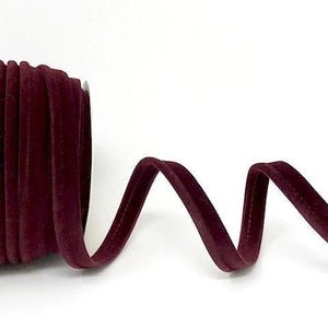 May include: A roll of burgundy velvet ribbon, partially unrolled, against a white background. The ribbon is a deep, rich colour, with a soft, velvety texture. The ribbon is approximately 0.64 cm wide.