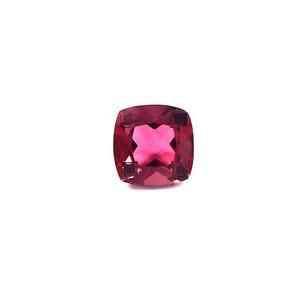 May include: A cushion-cut, faceted gemstone in a deep magenta hue. The gem has a square shape with rounded corners and a brilliant, reflective surface. The facets create a starburst pattern in the center, enhancing its sparkle against the white background.