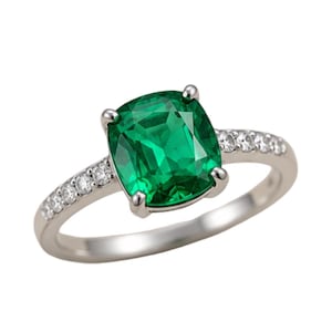 May include: A silver-toned ring featuring a large, cushion-cut vibrant green gemstone held by four prongs. The band is accented with a row of small, clear, round-cut stones embedded along each side of the shank, leading up to the center stone.