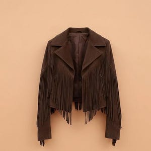 May include: A dark brown jacket featuring long fringe detailing across the chest, back, and sleeves. The jacket has a wide collar, long sleeves, and a cropped hemline. The material has a matte, suede-like texture throughout the entire garment.