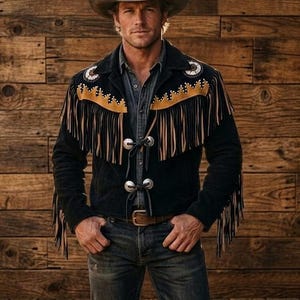 Könnte beinhalten: Eine Person trägt einen Cowboyhut, ein Jeanshemd und Jeans. Er trägt eine schwarze Wildlederjacke mit beigefarbenen Fransen und dekorativen Nähten. Die Jacke hat silberfarbene Knopfverschlüsse. Der Hintergrund ist eine Holzwand.