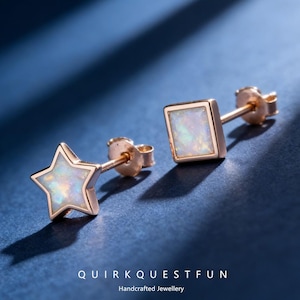 May include: A pair of stud earrings with a star and square design. The earrings have a gold-colored frame and feature an iridescent, opal-like center. The earrings are displayed on a blue surface. The text "QUIRKQUESTFUN Handcrafted Jewellery" is at the bottom.