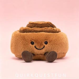 Peut inclure: Une peluche en forme de roulé à la cannelle avec un corps texturé marron clair et un dessus en spirale marron foncé. Elle possède deux petits yeux en perles noires, un sourire brodé noir et deux petits pieds en velours côtelé marron foncé.