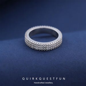 May include: A silver ring with three rows of small, clear gemstones. The ring is set against a dark blue background. The text "QUIRKQUESTFUN" and "Handcrafted Jewellery" are at the bottom of the image.