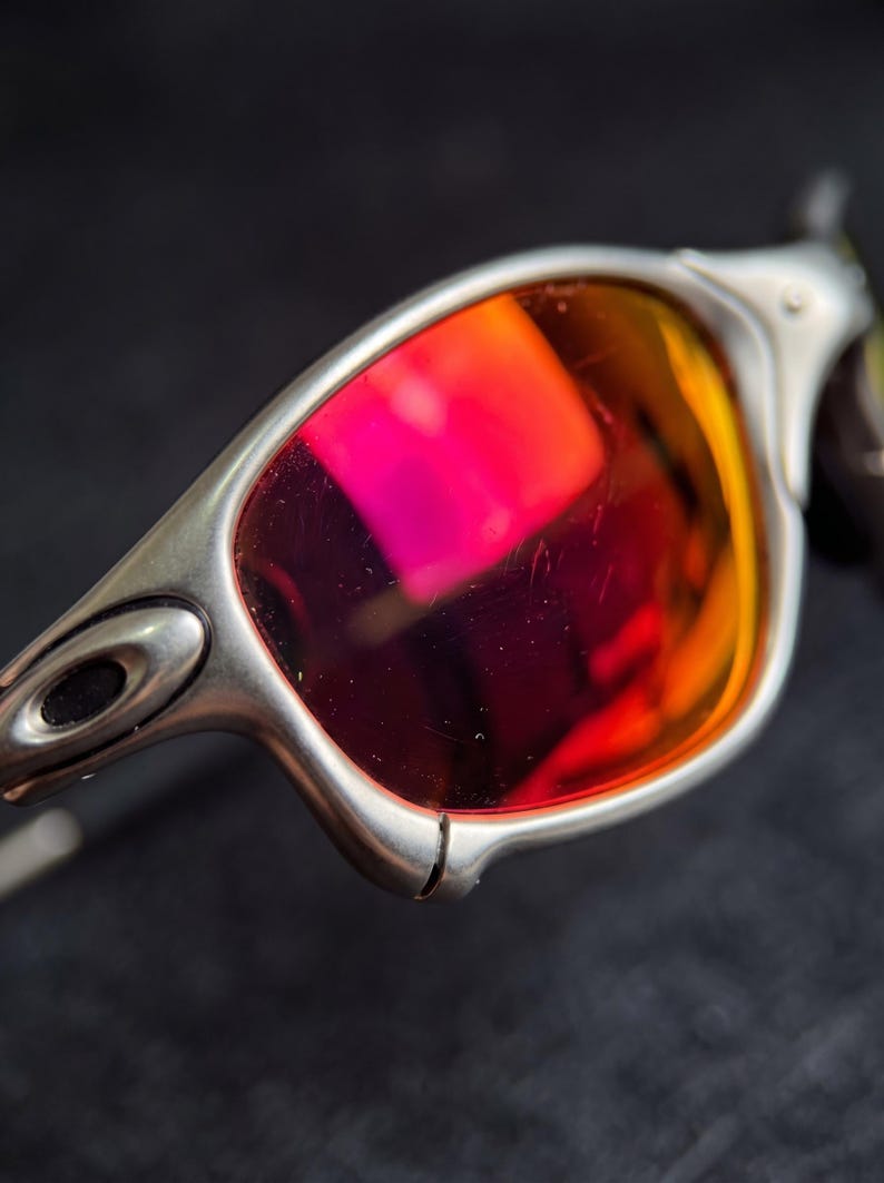 K&ouml;nnte beinhalten: Nahaufnahme einer Sonnenbrille mit silbernem Rahmen und leuchtend roten und orangen Gl&auml;sern. Die Gl&auml;ser reflektieren das Licht und erzeugen einen farbenfrohen Farbverlauf. Die Sonnenbrille hat ein schlankes, modernes Design.