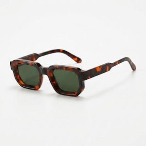 Peut inclure: Lunettes de soleil en écaille de tortue avec une monture géométrique et des verres vert foncé. Les lunettes de soleil présentent un motif marron et noir et sont posées sur un fond blanc.