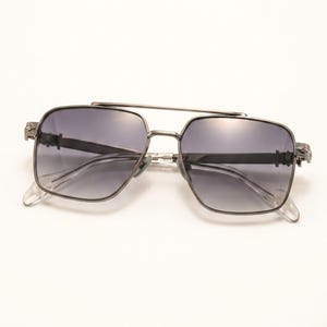 May include: Silver-framed sunglasses with a double bridge and gradient lenses. The square frames have decorative detailing on the temples and clear nose pads. The lenses transition from dark at the top to lighter at the bottom.