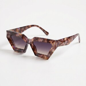 May include: Geometric sunglasses in a tortoiseshell pattern. The frames have an angular design, and the lenses have a gradient from dark purple to a lighter shade. The sunglasses are set against a white background. A stylish accessory.