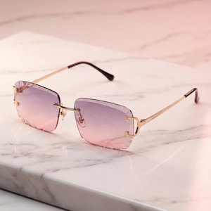 Può includere: Occhiali da sole senza montatura con una tinta sfumata rosa e viola. Le lenti rettangolari sono inserite in una montatura in metallo color oro con un design sottile e dritto. Le aste sono marrone scuro. Gli occhiali da sole sono esposti su una superficie di marmo bianco.