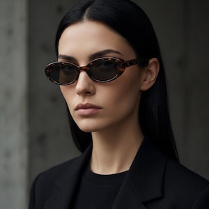 Peut inclure: Lunettes de soleil ovales avec un motif écaille de tortue. Les lunettes ont des verres foncés. La monture est de couleur marron chaud avec des taches plus foncées.