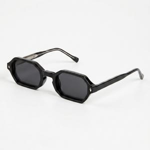 Peut inclure: Lunettes de soleil noires avec une monture octogonale. Les verres sombres sont de forme géométrique. Les branches sont fines et noires. De petits accents argentés sont visibles sur la monture. Sur fond blanc.