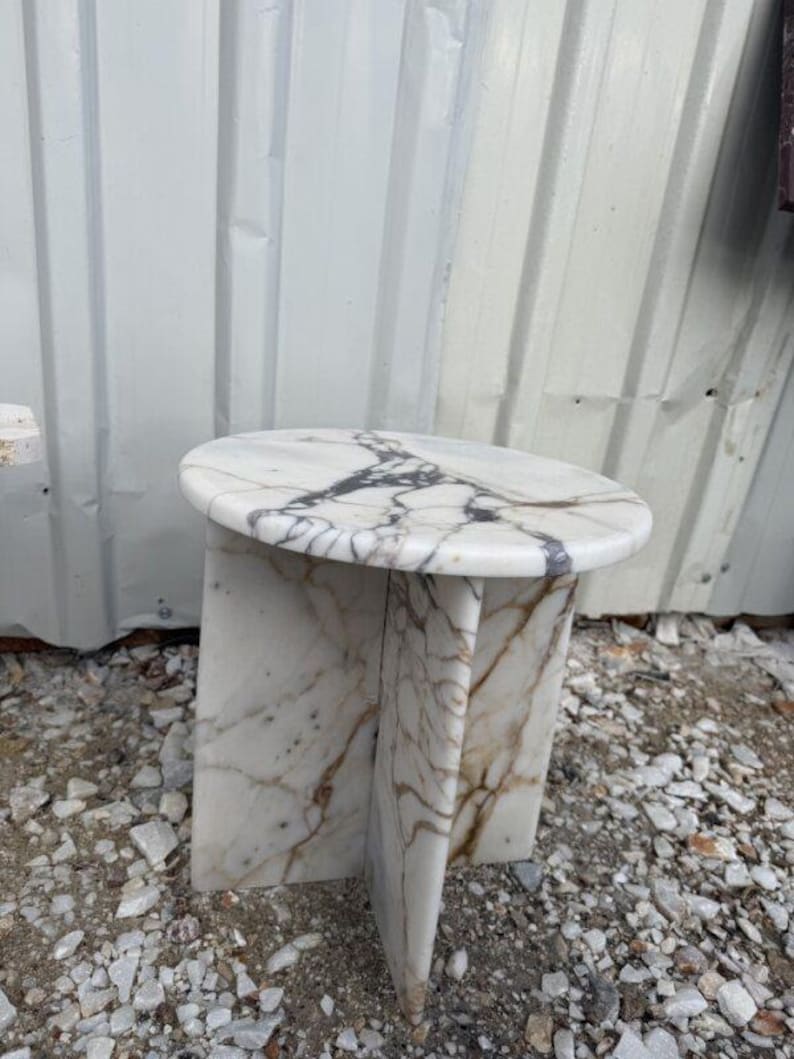 Puede incluir: Una mesa auxiliar de m&aacute;rmol blanco con una tapa redonda y un dise&ntilde;o de base &uacute;nico. La mesa presenta vetas grises oscuras y marrones en todo el m&aacute;rmol. Una pieza de acento elegante para cualquier habitaci&oacute;n.